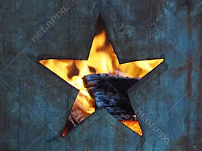 Hole in the shape of a five-pointed star cut into a metal burning barrel with flames and burned wood visible inside