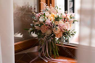 Pink and peach wedding bouquet stands on the windowsill
