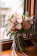 Pink and peach wedding bouquet stands on the windowsill