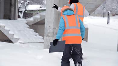 Construction worker and engineer talking on a construction site. Workers in helmets outside the building