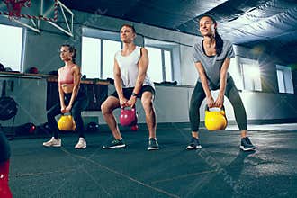 The strong young fitness men and women in sportswear doing exercises at gym