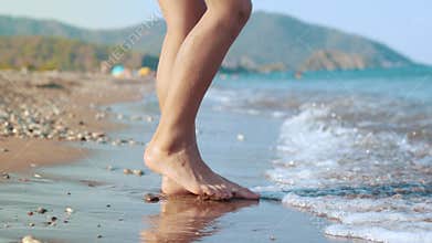 Girl touching sea water by foot. Female foot touching water wave at sea beach