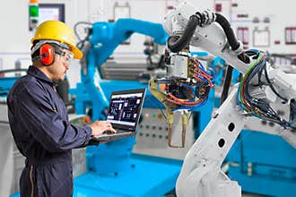 Engineer using laptop computer maintenance automatic robotic hand machine tool in automotive industry, Industry 4.0 concept
