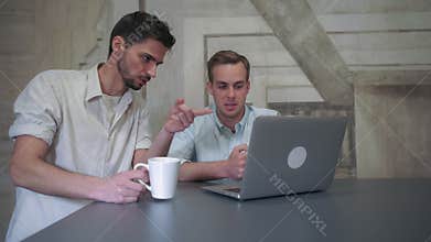 Two young man in the coffee house looking on the screen computer and talking.