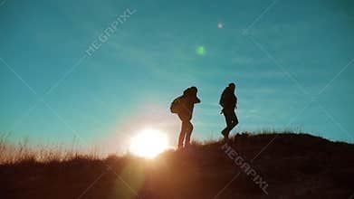 Teamwork. Two hikers enjoying sunrise from top of a mountain and dog. Two hikers with backpacks climbing a peak on cloud