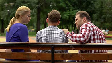 Parents talking with son on bench in park, supporting teen in time of trouble