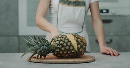 In the kitchen a woman cut a big pineapple with a big knife closeup, slow motion.