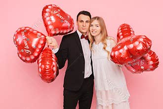A loving couple, a man and a woman, holding heart-shaped balloons, in a studio on a pink background, concept for Valentine`s Day