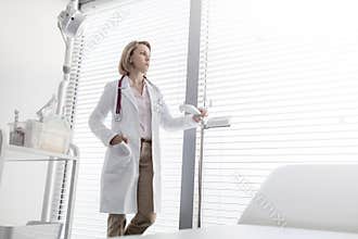 Thoughtful mature doctor standing by measurement scale while looking through window at hospital