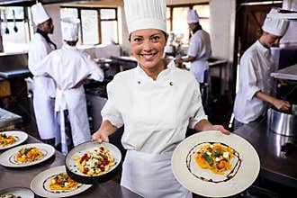 Female chef holding plate of prepared pasta in kitchen