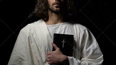 Monk in white robe holding holy bible against dark background, Christianity