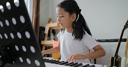 Asian little girl learning to play basic piano by using electric synthesiser keyboard for beginner music instrumental self studyin