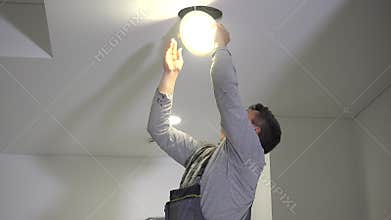 Skilled electrician man connect wires to led light panel and mount into ceiling