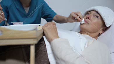 Nurse of mental hospital feeding indifferent woman with porridge, asylum