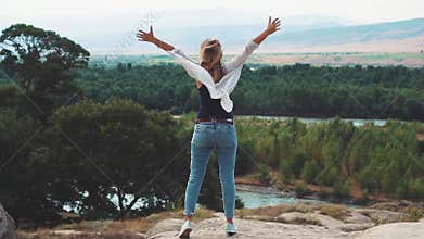 Feeling of freedom and happiness, a sweet and slender young woman standing on a cliff, and raising her arms upwards