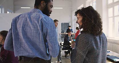 Camera follows two happy young multiethnic business managers walking together along modern office talking and smiling.