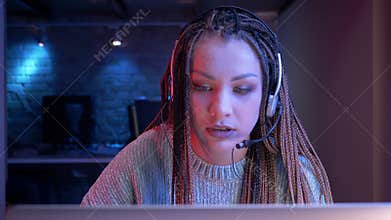 Closeup shoot of young attractive female blogger with dreadlocks in headphones playing video games and streaming live
