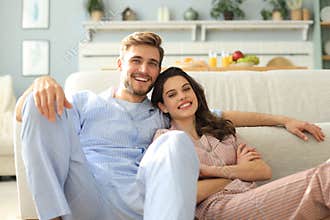 The happy couple in pajamas sitting on the floor background of the sofa in the living room