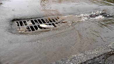 Havy rain in a city, flooded street and manhole cover of storm drain.