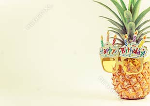 Yellow fancy glasses on fresh pineapple, copy space on left, summer birthday concept, pastel color