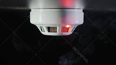 Smoke detector on a black background. There are trickles of smoke. The sensor is triggered - the red alarm indicator