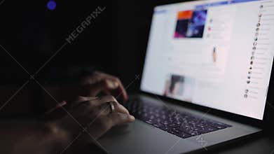 Man is working typing use laptop computer at home office at dark night. Social media facebook browsing