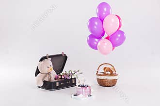 Birthday cake, teddy bear in vintage suitecase and balloons on white background