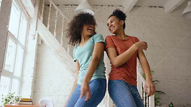 Mixed race young beautiful girls dancing on a bed together having fun leisure in bedroom at home