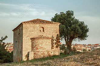 a lonely ancient chapel under a tree on the hill of the sea coast in a coastal Greek village at dawn of the day