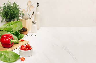 Healthy vegetarian ingredients for spring fresh green salad and kitchenware in white elegant kitchen interior.