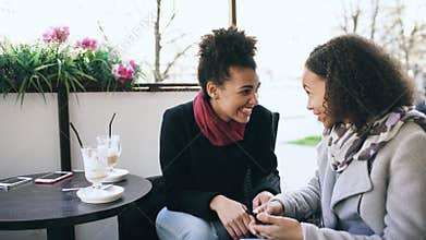 Two attractive mixed race women talking and drinking coffee in street cafe. Friends have fun after visiting mall sale