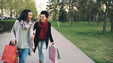 Two attractive mixed race women dancing and have fun while walking down the park with shopping bags. Happy young friends