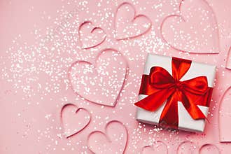 Gift box and paper hearts with sparkling glitter on pink background. Romantic st. Valentine`s day concept of greetings. Top view,