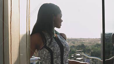 An elegant dark-skinned young girl stands on the balcony and admires the view