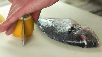 Hands cutting lemon, raw fish.