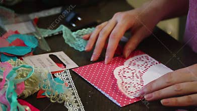 The girl is engaged in making greeting cards at home. Using paper, lace, braid and other materials.
