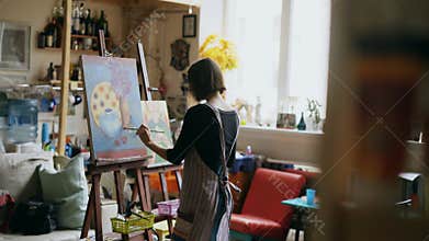 Rear view of Young painter girl in apron painting still life picture on canvas in art-class