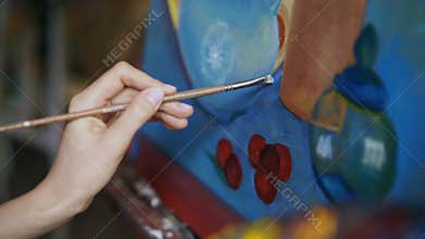Close-up of artist woman with brush painting still life picture on canvas in art-class