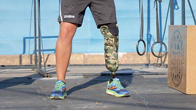 Strong arms of male handicapped with prosthetic leg in form of sport raises heavy weight