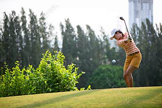 Asian woman golf player hitting chips golf ball to the hole on the green with golf club in the sunny day, copy space.
