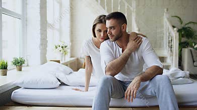 Depressed yong man sitting in bed having stressed while his girlfriend come and embrace him and kiss in bedroom at home