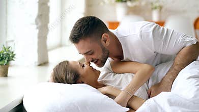 Young beautiful and loving couple wake up at the morning. Attractive man kiss and hug his wife in bed