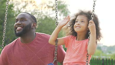 Happy daughter and daddy swinging in yard and waving hands to mom, family