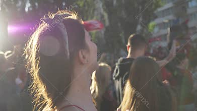 Young beautiful woman lifting hands and cheering up on street during festival, happy, crowd of fans standing around