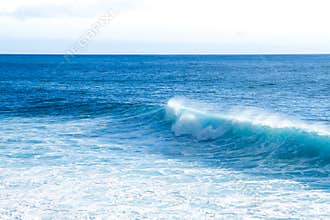 Waves braking close to the beach shore with blue turquoise ocean water and resulting white foam