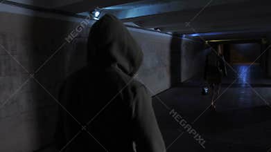 Man in hoodie chasing woman in dark tunnel