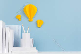 School template - white books, stationery, decorative paper yellow lightbulbs origami on white desk and soft blue background.