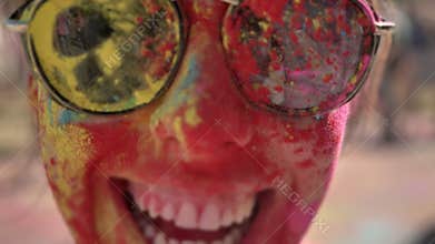 Face of young happy girl in colourful powder with sunglasses is smiling on holi festival in daytime in summer, color