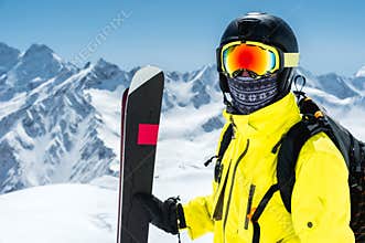 A large portrait of a skier in a protective helmet and glasses - a mask and a scarf next to the skis against the snow