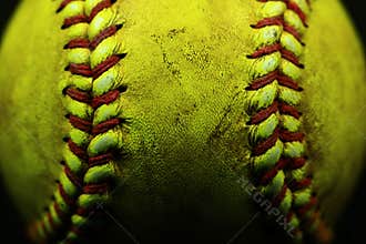 Yellow softball closeup with red seams on black background.